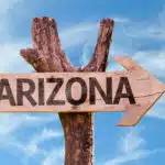 wooden stick post with a wooden arrow sign with arizona written on it pointing to the right