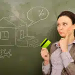 Closeup portrait of pretty young business woman against green board holding credit card and drawing beautiful house with backyard. Mortgage concept