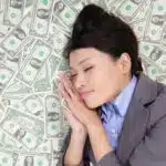 Image of woman in a business suit sleeping on a bed of money