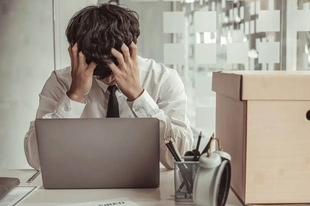 Man in a suit sitting behind a laptop with his head resting in his hands in frustration