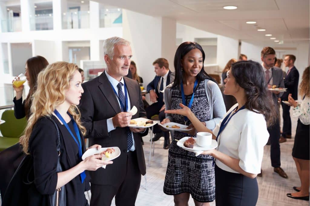 four business people standing together chatting while eating food