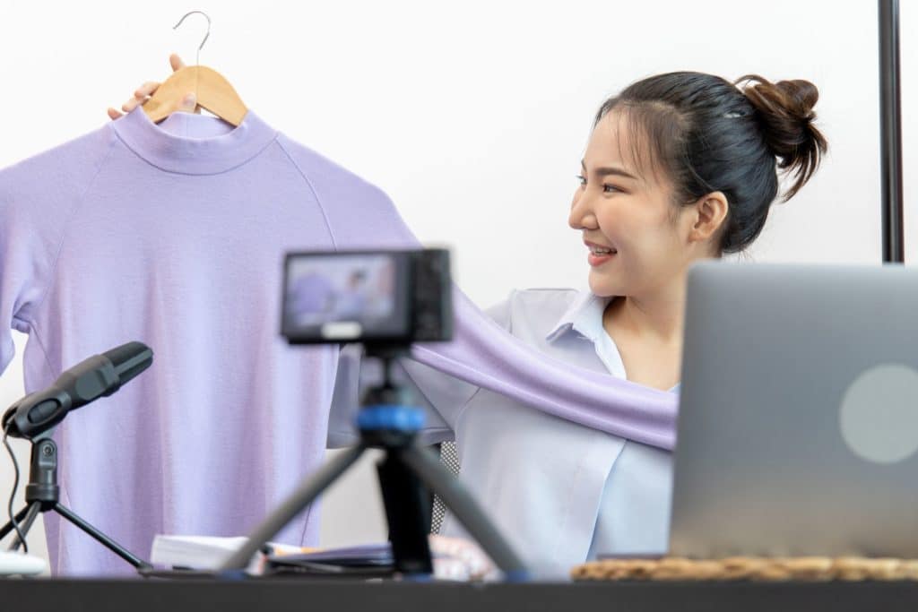 young woman filming a video while holding an item of clothing in her right hand