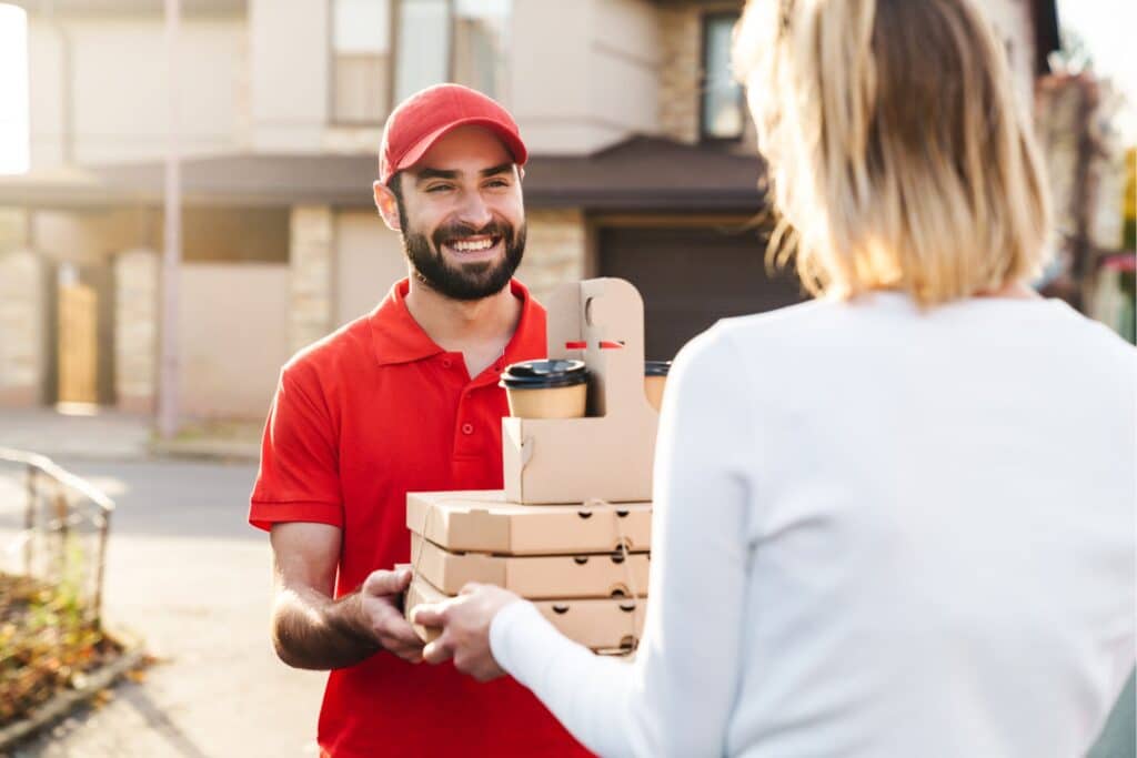 A food delivery driver handing out boxes of food to a woman in her driveway