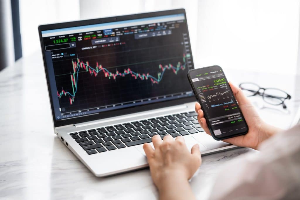 person trading stocks on a laptop and mobile phone
