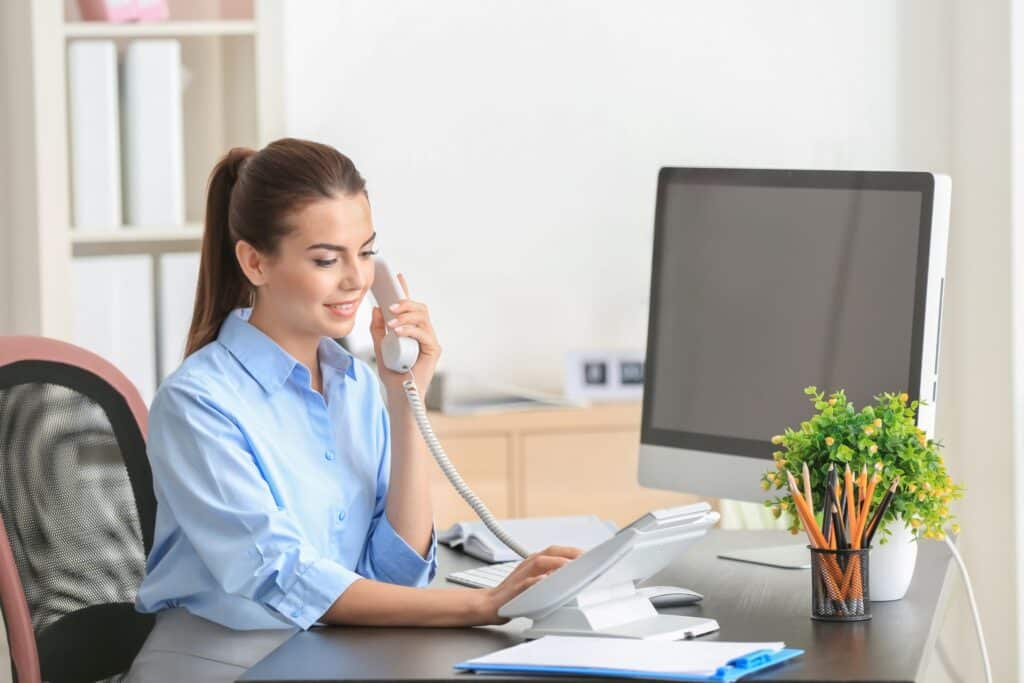 Woman sitting at a desk in an office dialing a number on the telephone 