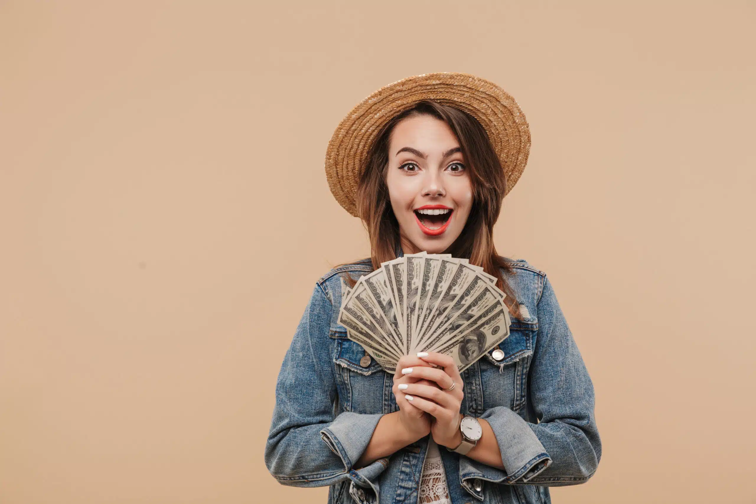 Portrait of a smiling young girl in summer clothes showing money banknotes and looking at camera isolated over beige background for the concept "What is passive income?"